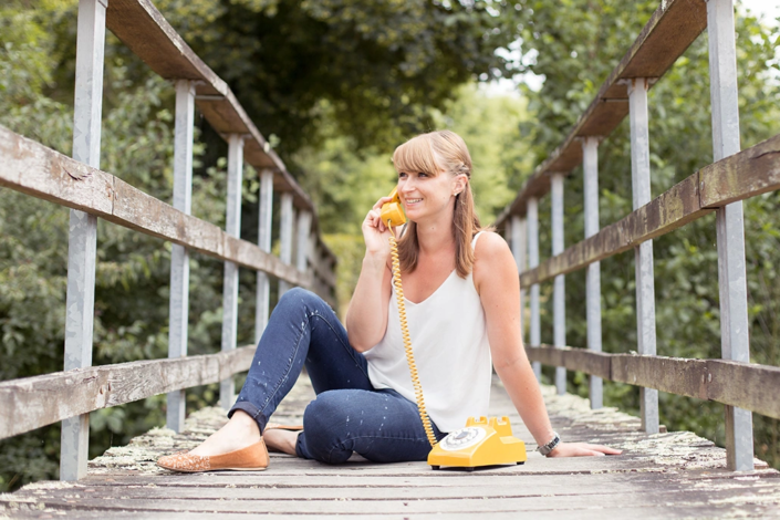 femme assise sur un pont en bois utilisant un téléphone a cadran