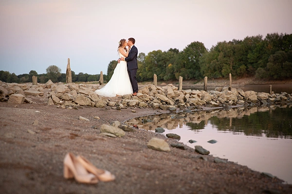 mariés vue de loin au bord de l'eau avec les chaussures de la mariés au premier plan